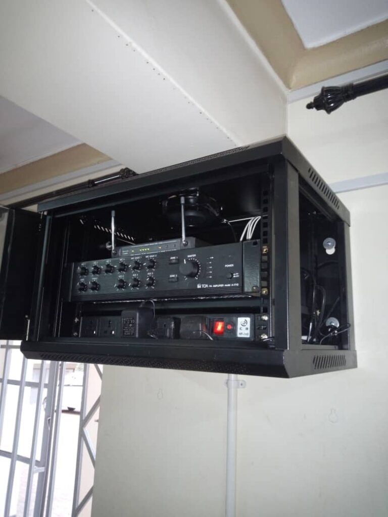 Wall-mounted rack with TOA amplifier and wireless microphone receiver at Mengo Senior School